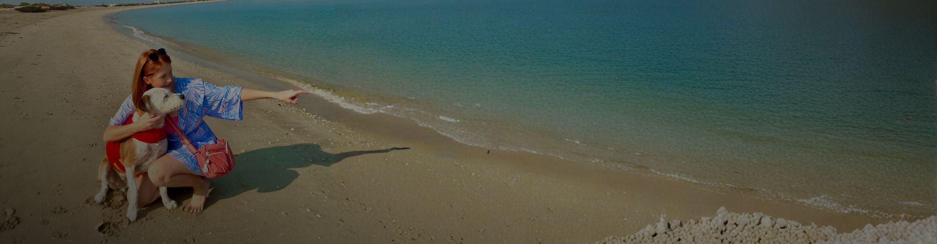Carmen sitting on the beach pointing toward the sea while her dog Marty sits beside her.